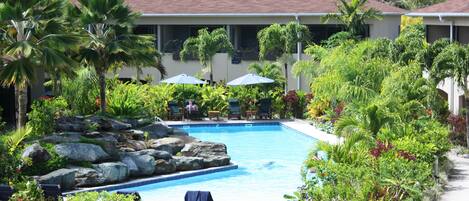 A pool area with lounge chairs, umbrellas, and a building with a red roof.