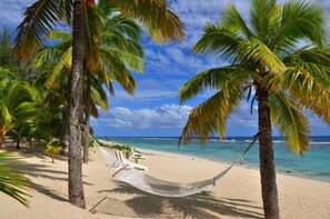 Una playa con palmeras, una hamaca y un cielo azul despejado.