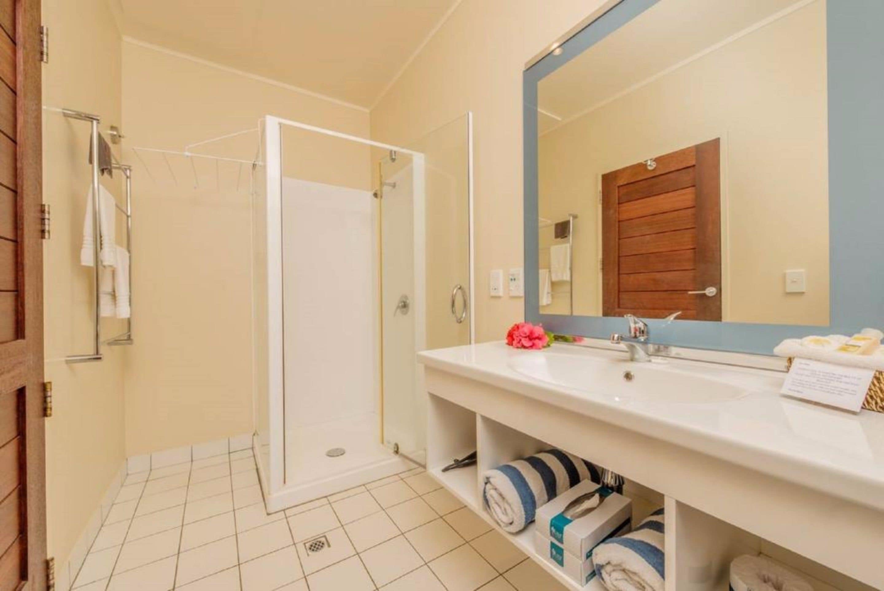 A bathroom with a white sink, a mirror, a shower, and a towel rack.