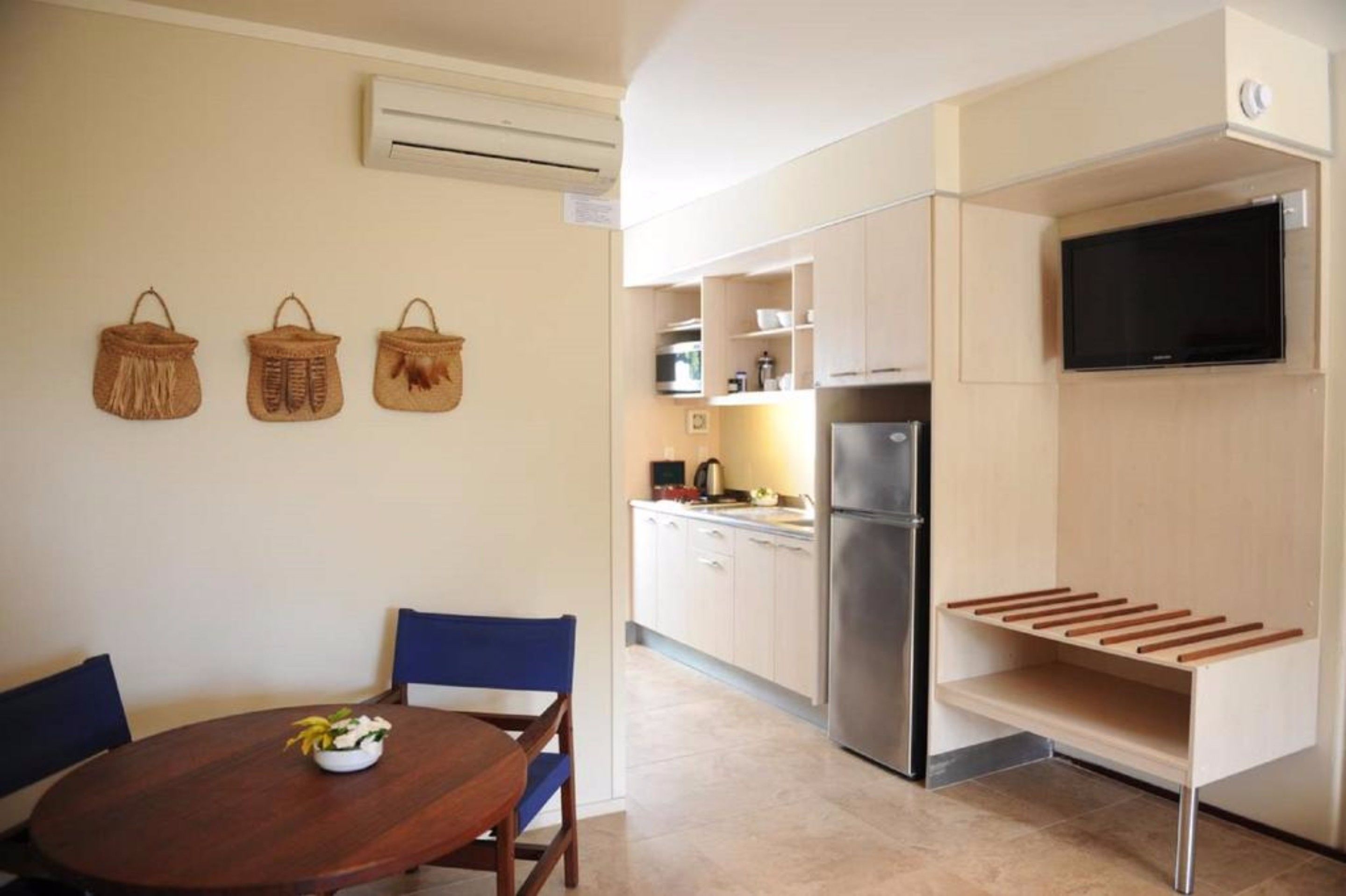 Une cuisine compacte dotée d’un réfrigérateur encastré, d’une table à manger avec des chaises et d’un téléviseur fixé au mur.