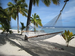 A hammock on a sandy beach with palm trees and the ocean in the background.