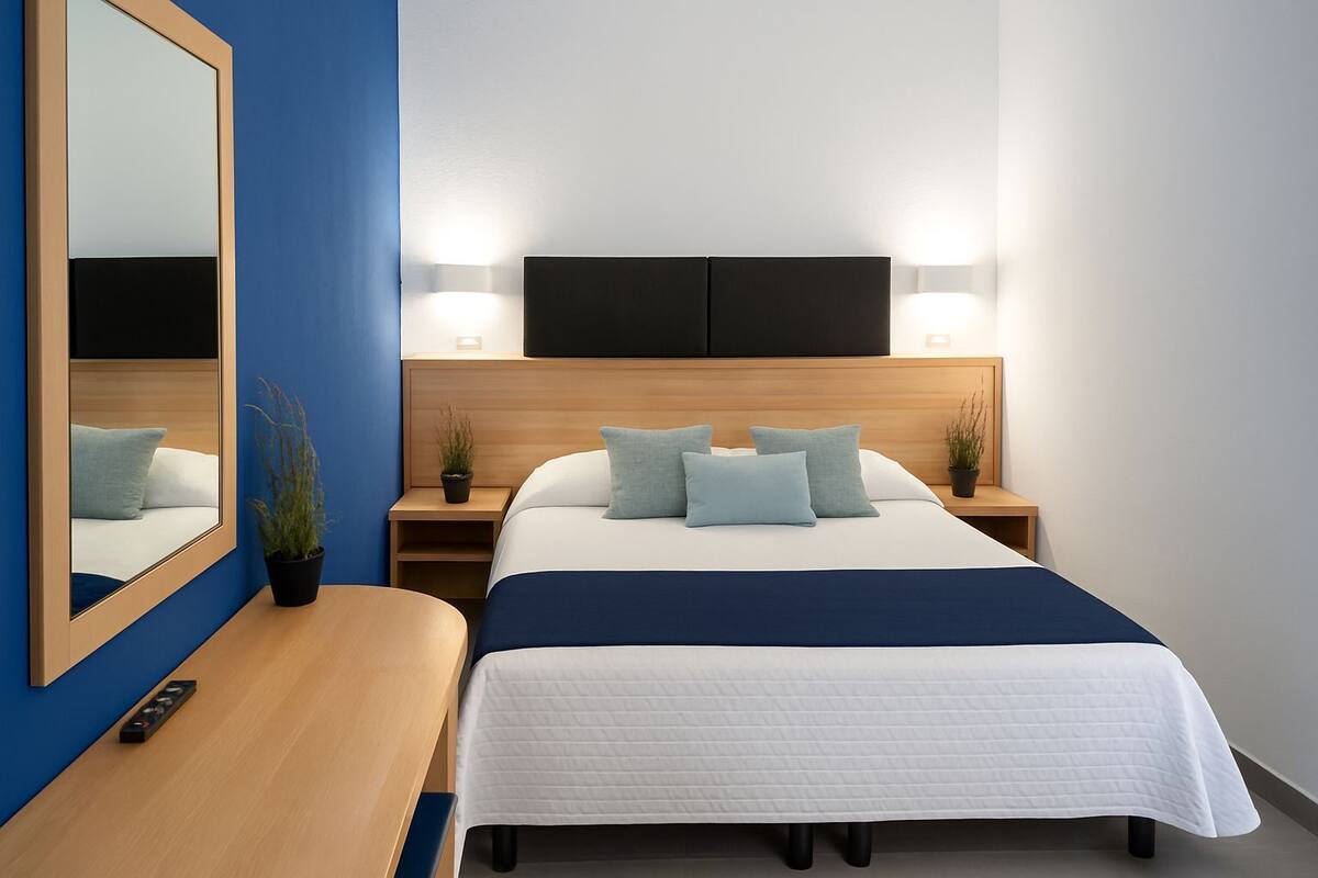 A modern hotel room with a large bed, bedside tables, a mirror, and a flat-screen TV.