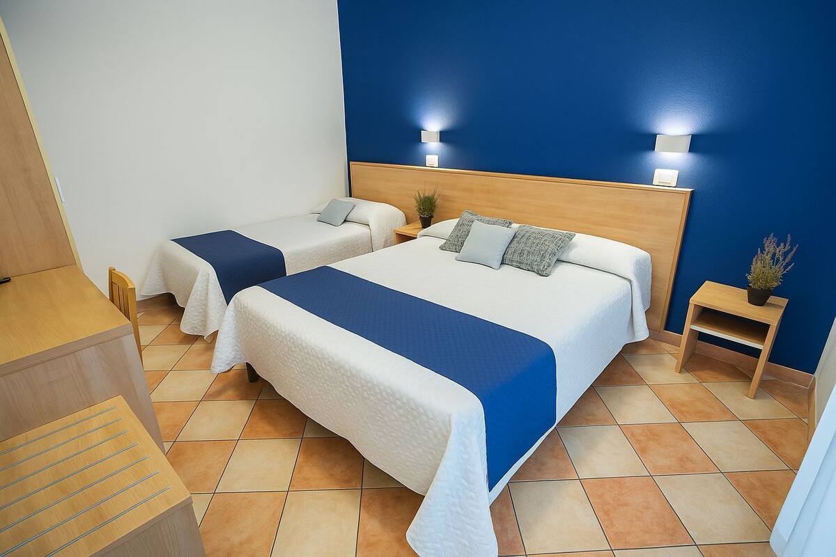 A hotel room with two beds, a wooden nightstand, a small table, and a potted plant.