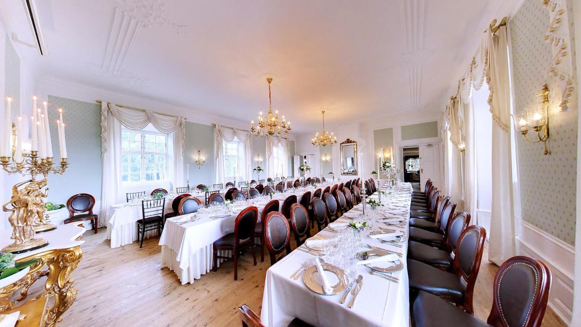 Un comedor formal con mesas largas, candelabros y decoración elegante.