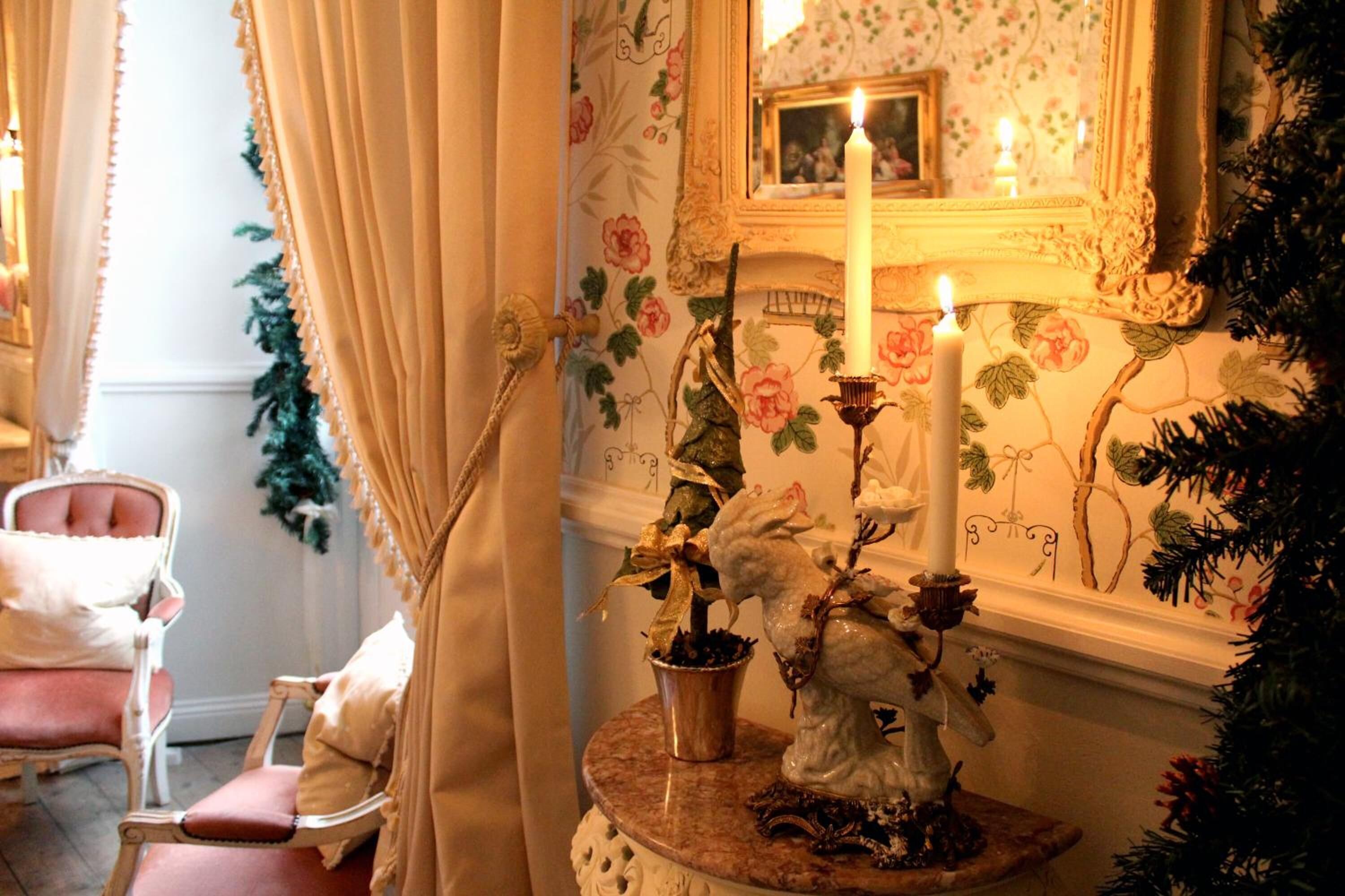 Une pièce avec un papier peint à motifs floraux, une table ronde avec une bougie et une chaise.