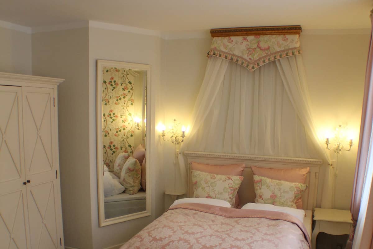 A bedroom with a bed, a chair, a nightstand, a mirror, and a wardrobe.