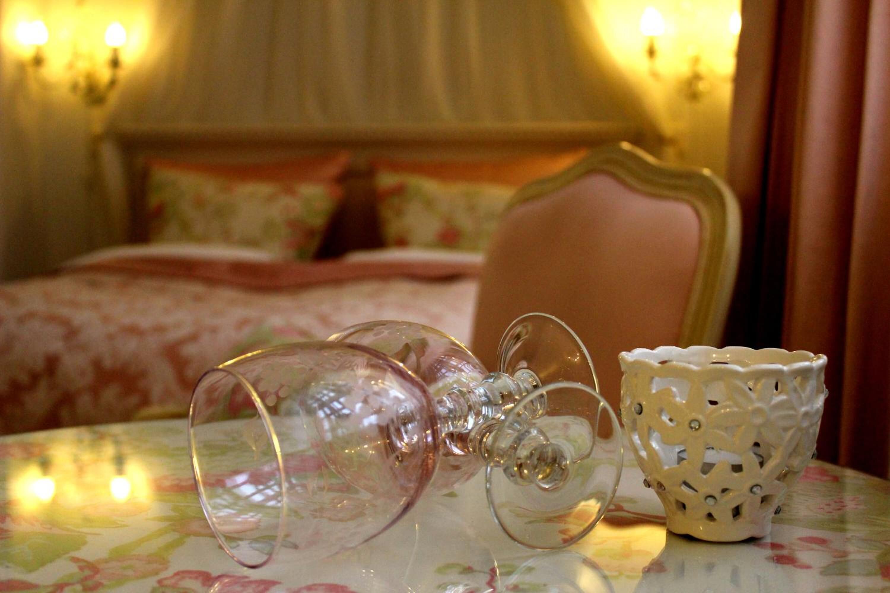 A bedroom with a bed, a table with a glass object and a decorative bowl, and wall sconces.