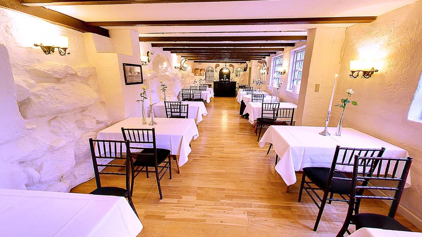 A long dining hall with tables and chairs, wooden floors, and stone walls.