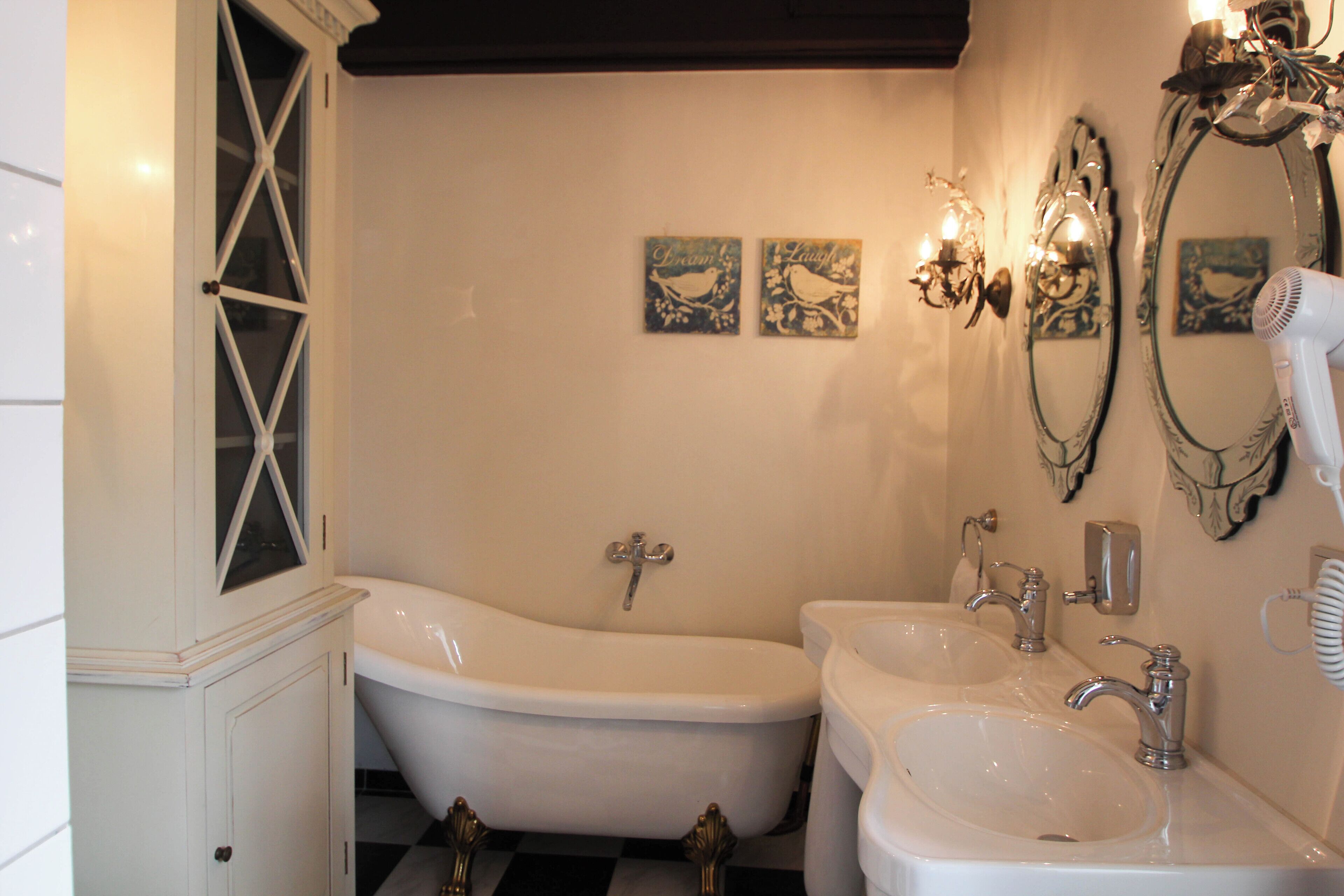 A bathroom with a freestanding bathtub, two sinks, and decorative wall sconces.