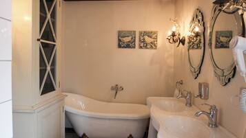 A bathroom with a freestanding bathtub, two sinks, and decorative wall sconces.