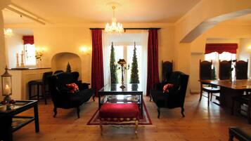 Un salón tradicional con un banco tapizado rojo, dos sillones negros, una mesa de centro de madera y una araña.