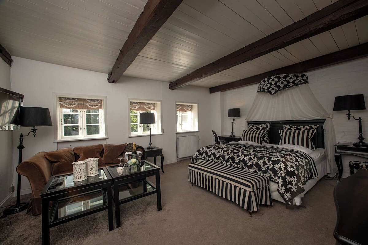 A bedroom with a bed, a sofa, a table, and two windows.