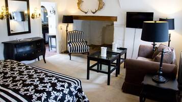 Una habitación de hotel con cama, chimenea, sillón a rayas, sofá marrón, lámpara negra y televisor.