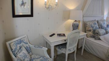 A room with a white bed, a white desk, a white chair, a chandelier, and a framed picture on the wall.
