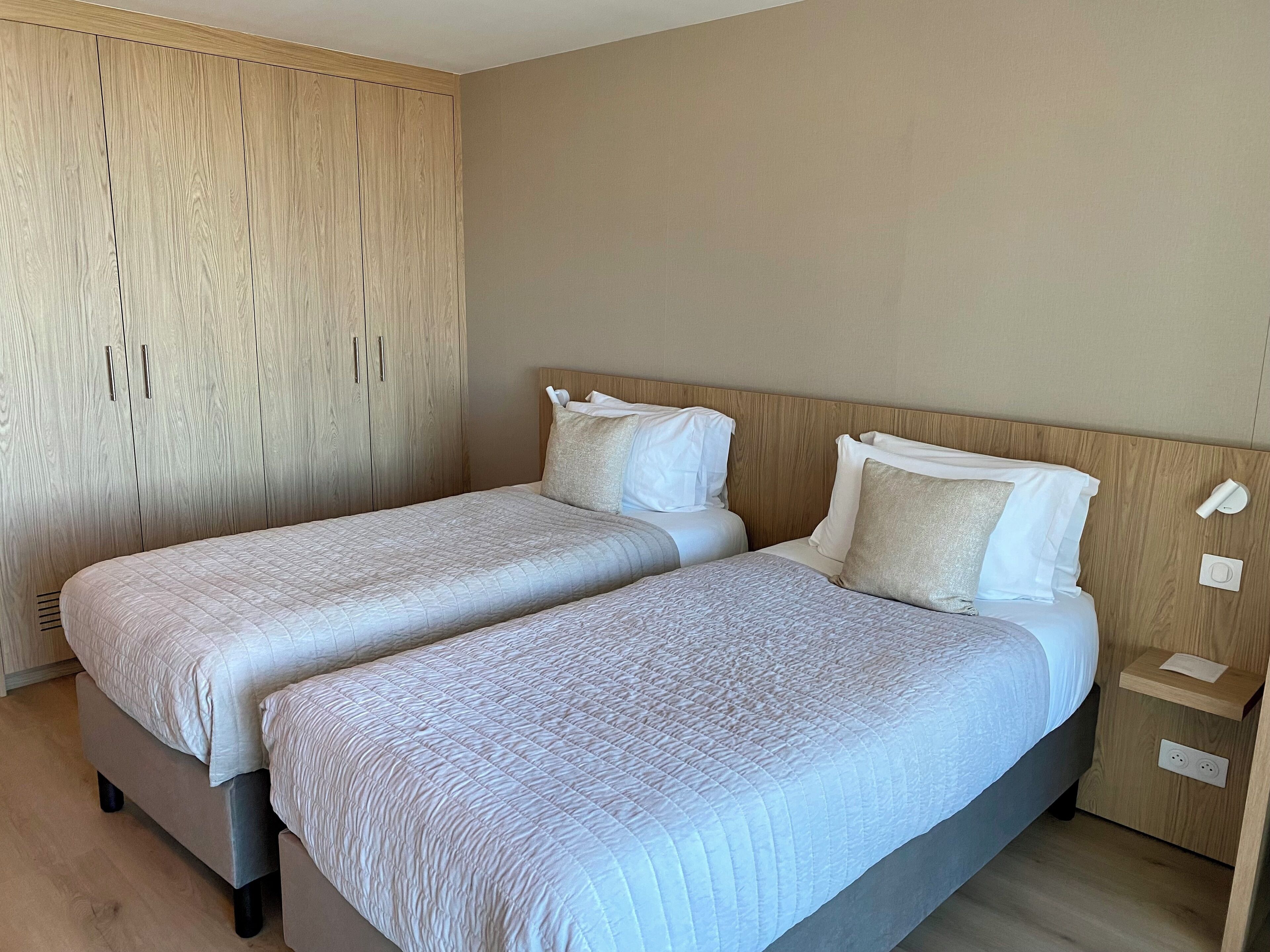 Una cama doble con cabecera de madera, un armario de madera y una mesita de noche con lámpara.