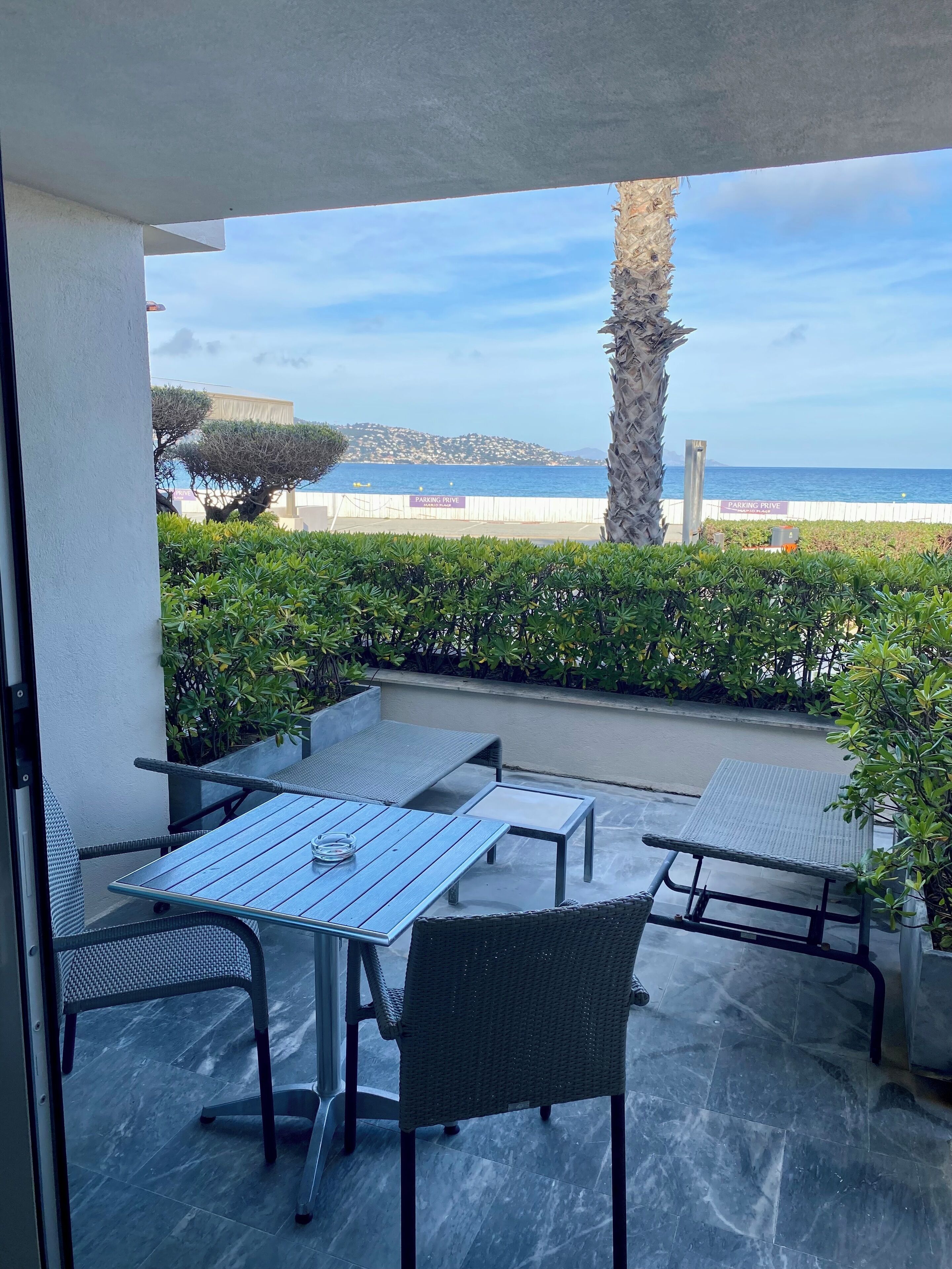 A patio with outdoor furniture, a view of the sea, and a "PARKING DRIVE" sign.