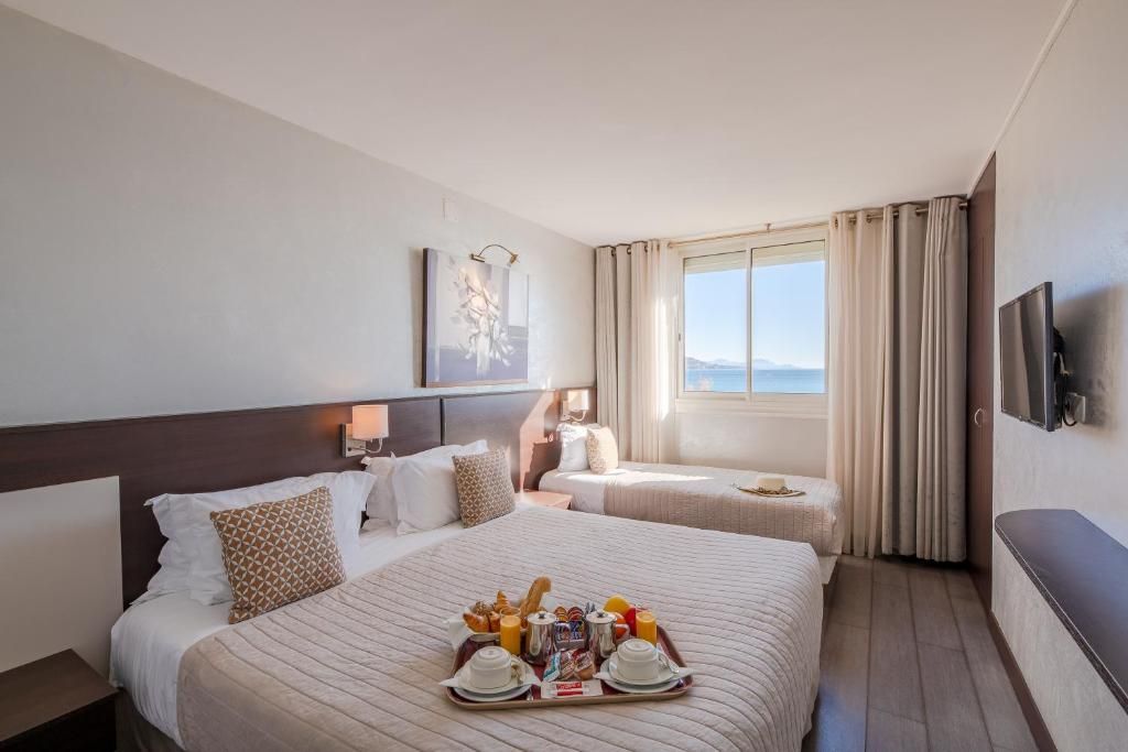 Une chambre d’hôtel avec deux lits, une table à manger avec un petit-déjeuner, une télévision et une fenêtre avec des rideaux.