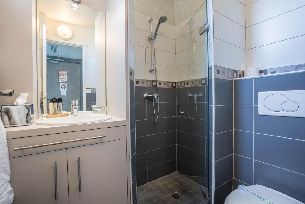 A modern bathroom with a glass shower enclosure, a sink with toiletries, and a toilet with a bidet attachment.