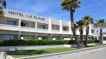 A hotel named "HOTEL LA PLAGE" with a modern design, multiple balconies, and palm trees in the foreground.