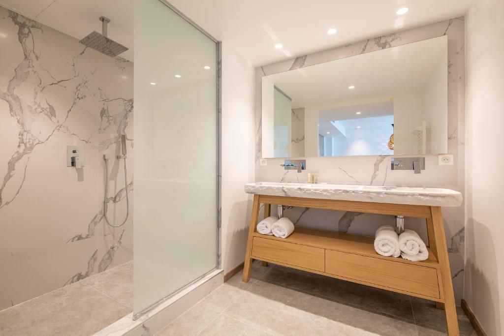 A modern bathroom with a marble vanity, a glass shower enclosure, and a large mirror.