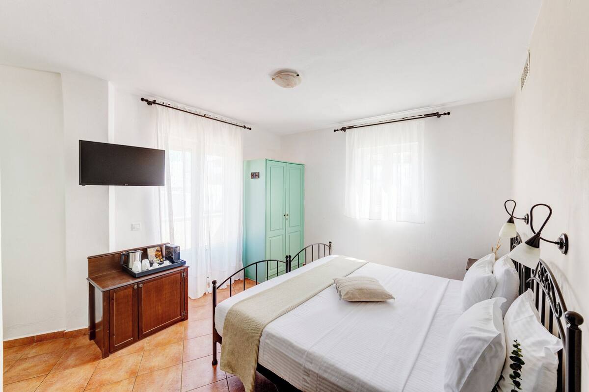 A bedroom with a bed, a wardrobe, a television, and a window with curtains.
