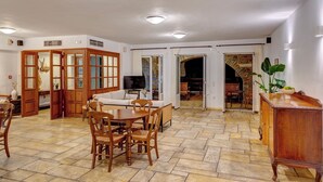 A spacious dining area with a wooden table and chairs, a television, and a stone-tiled floor.