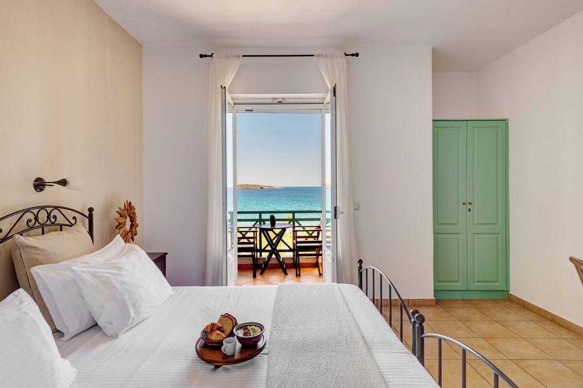 A bedroom with a bed, breakfast tray, and a view of the sea through an open door.