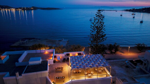 A rooftop terrace with outdoor seating, overlooking a calm sea with boats.