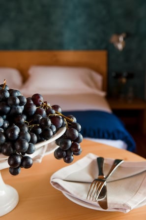 A bed with a wooden headboard, a bedside table with a white vase of dark grapes, and a folded white napkin with a fork on it. - Hotel Meublè Sertorelli Reit (Bormio)