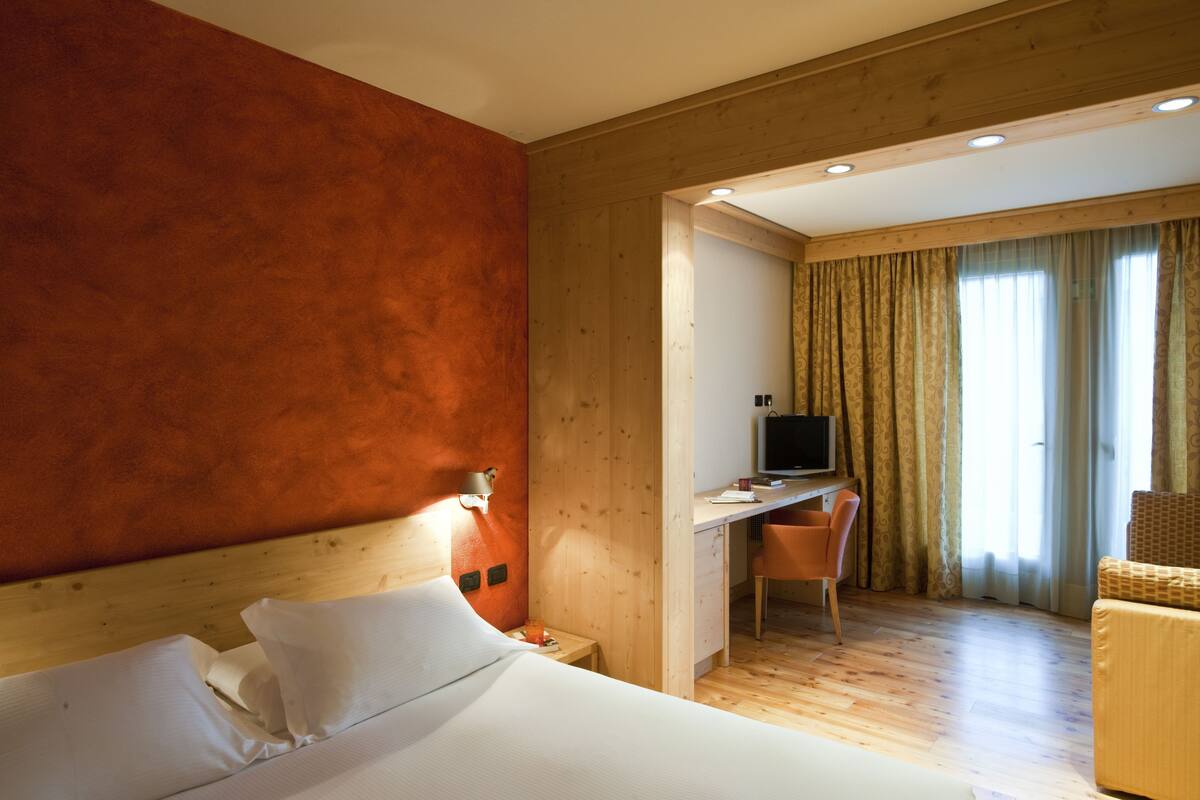 A hotel room with a wooden headboard, a bed with white linens, a desk with a computer, a chair, and a television.