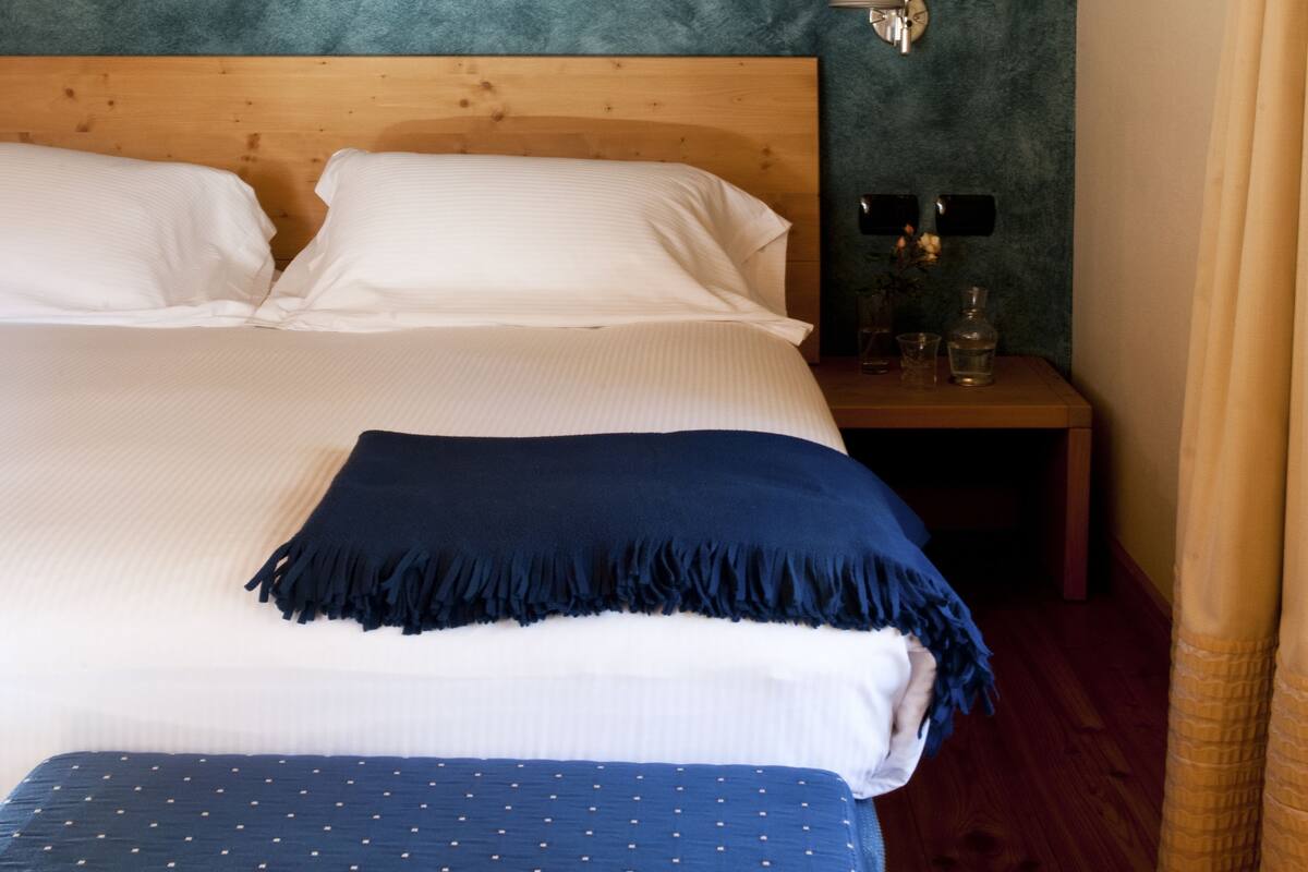 A neatly made bed with white and blue bedding, a wooden headboard, and a nightstand with a lamp and a vase.