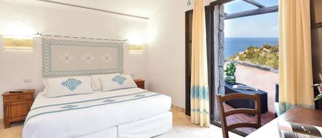 Un dormitorio con cama, mesitas de noche y vista al mar a través de un ventanal.