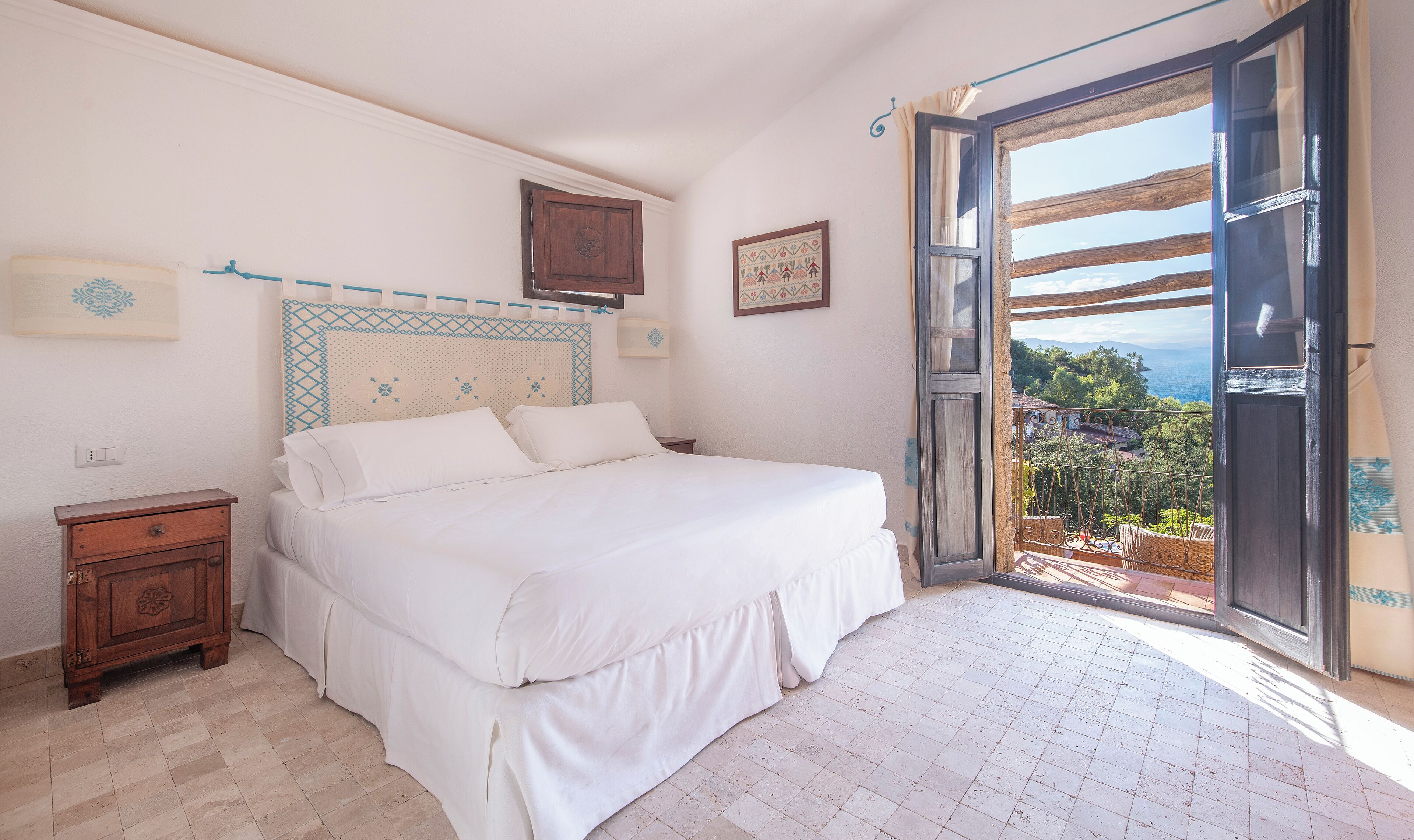 A bedroom with a large bed, a nightstand, a wooden cabinet, and a view of the outdoors through an open door.
