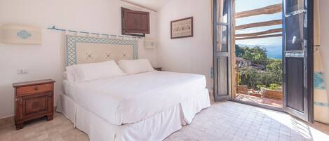 Un dormitorio con una cama grande, una mesita de noche, un armario de madera y vistas al exterior a través de una puerta abierta.