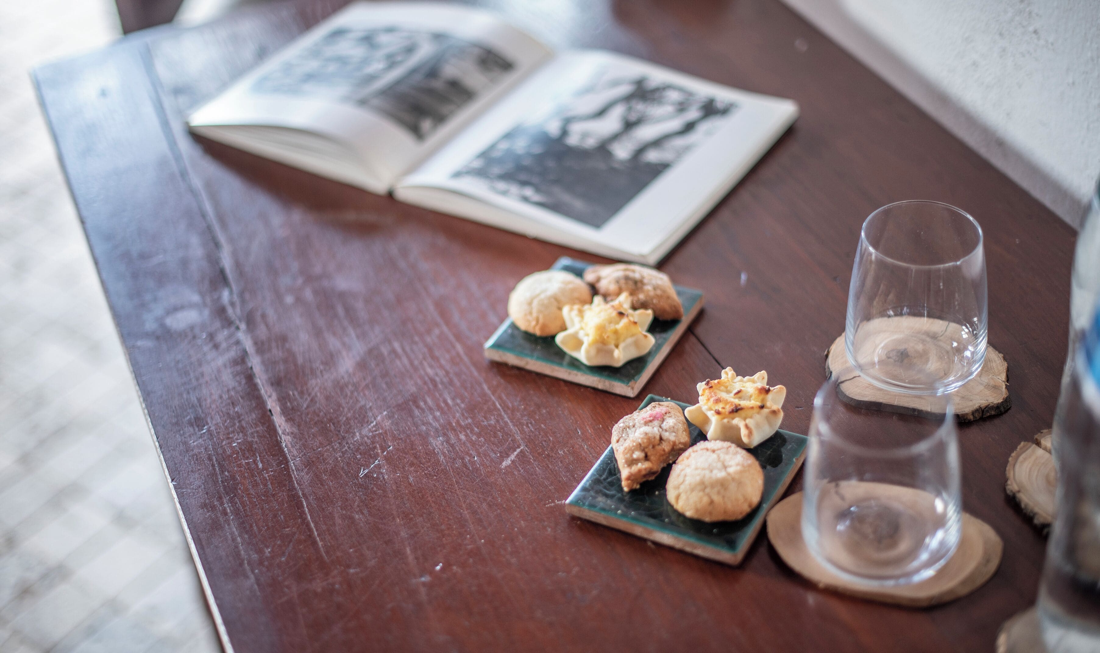 A wooden table with a book, two small plates with pastries, and a glass of water.