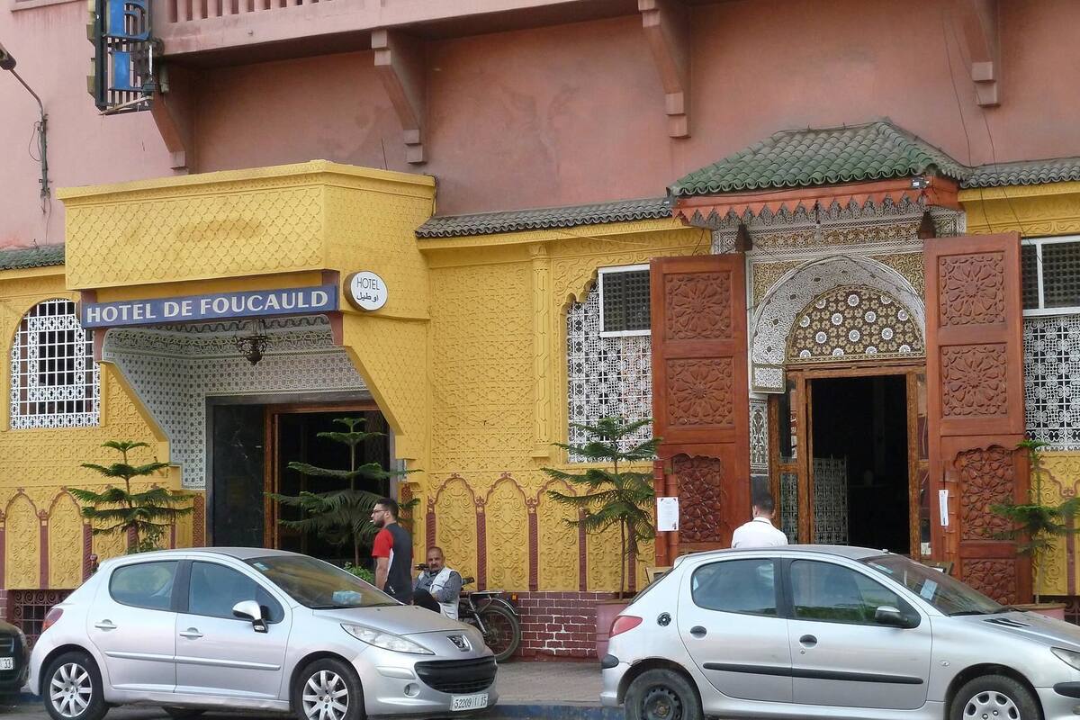 La façade d’un hôtel, ornée de détails architecturaux complexes, une enseigne indiquant « HÔTEL DE FOCAULD » et deux voitures garées.