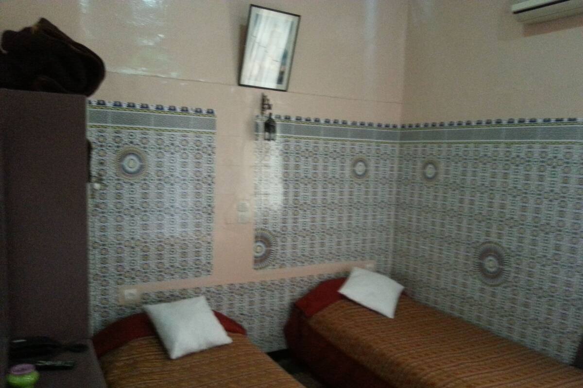 Une chambre avec deux lits, des murs à motifs, une petite table et un climatiseur fixé au mur.