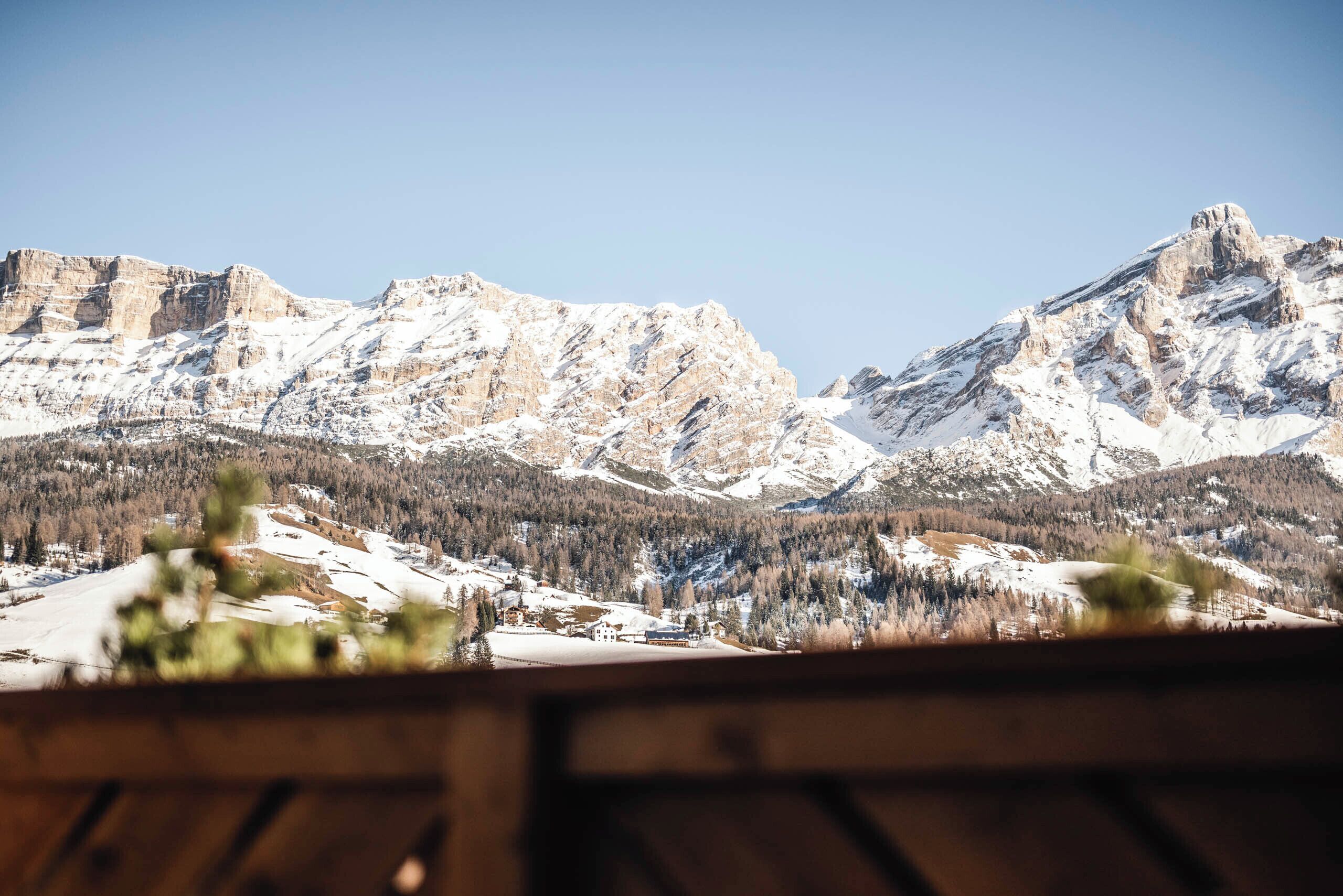 Paesaggio montuoso con cime innevate e una valle con edifici e alberi.