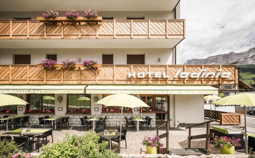 Un hotel con ristorante e bar per snack, posti a sedere all'aperto con ombrelloni e fioriere sul balcone.