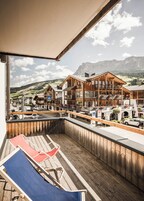 Um deck de madeira com cadeiras de descanso, com vista para uma paisagem montanhosa e uma fileira de edifícios de madeira com varandas.