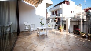 A sunlit patio with white chairs, a small table, and potted plants. - Cabrera House (Pozzallo)