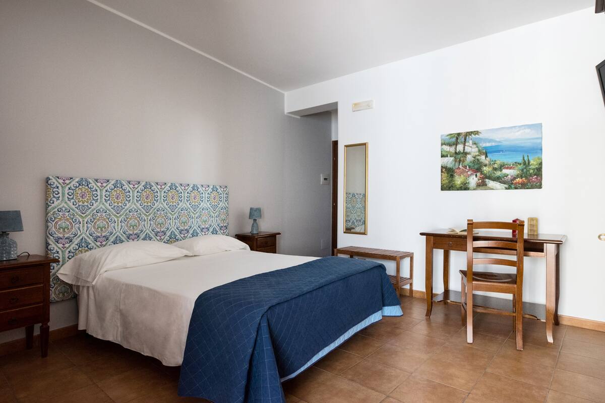 Une chambre à coucher comprenant un lit, un bureau, une chaise, une table de chevet, un miroir et un tableau accroché au mur.