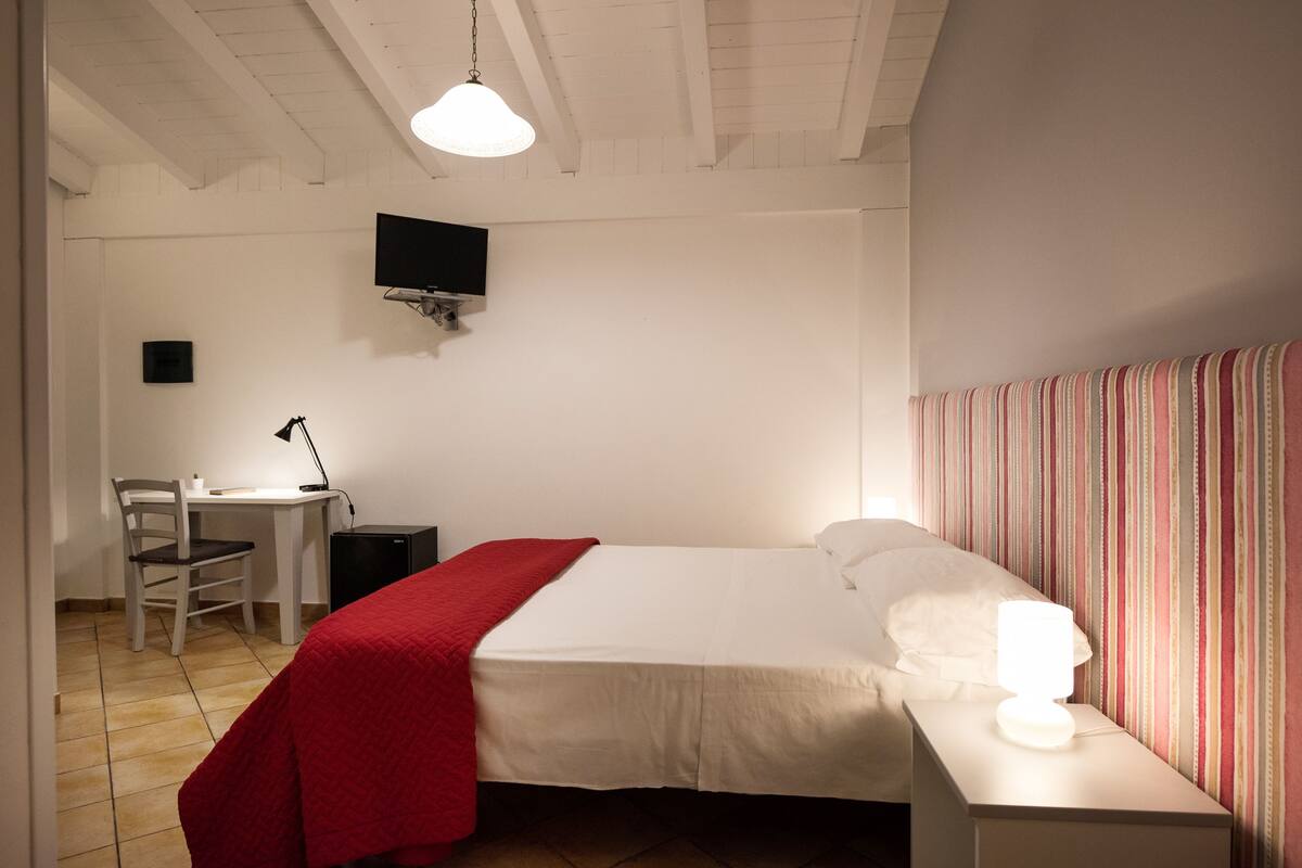 Une chambre à coucher comprenant un lit, un bureau, une chaise, un téléviseur fixé au mur et une lampe de chevet.