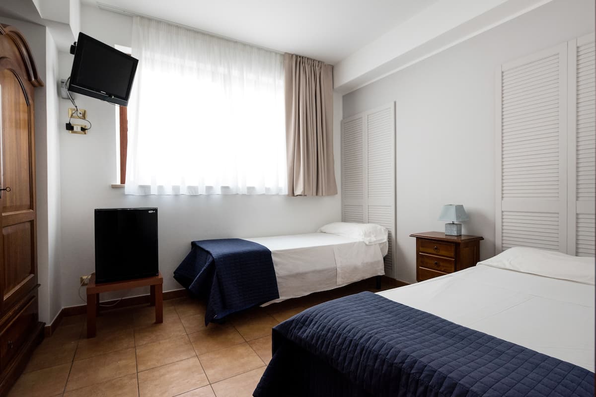 Une chambre d’hôtel comprenant un lit, un téléviseur posé sur un meuble, une table de chevet avec une lampe et une armoire.