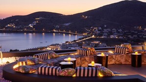 Una terraza en la azotea con mobiliario exterior, vistas al mar y edificios a lo lejos.
