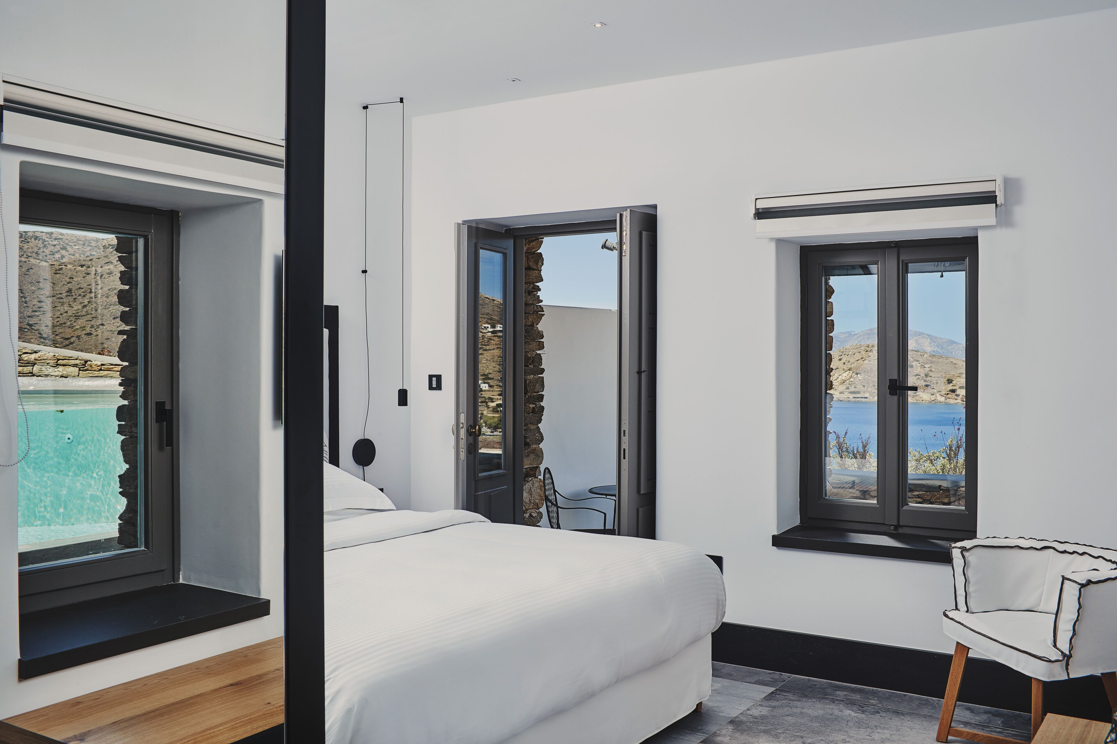 Un dormitorio con cama, una silla y vistas a una piscina y montañas a través de las ventanas.