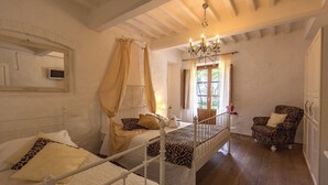 Une chambre avec deux lits, un lustre, un fauteuil à motifs léopard et une petite table sur laquelle est posé un vase.