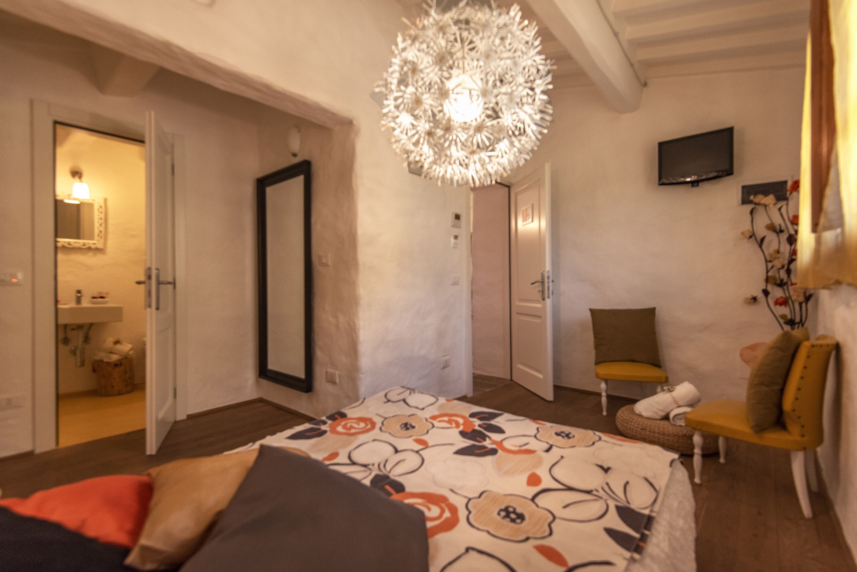 Une chambre à coucher comprenant un lit, une chaise, un téléviseur et une porte donnant sur une autre pièce.