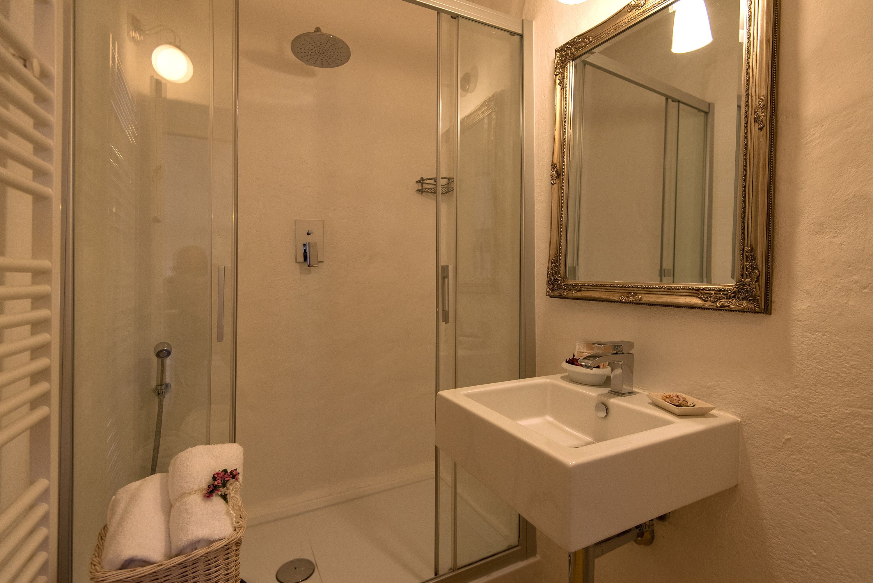 A bathroom with a glass-enclosed shower, a white sink, and a mirror with an ornate frame.