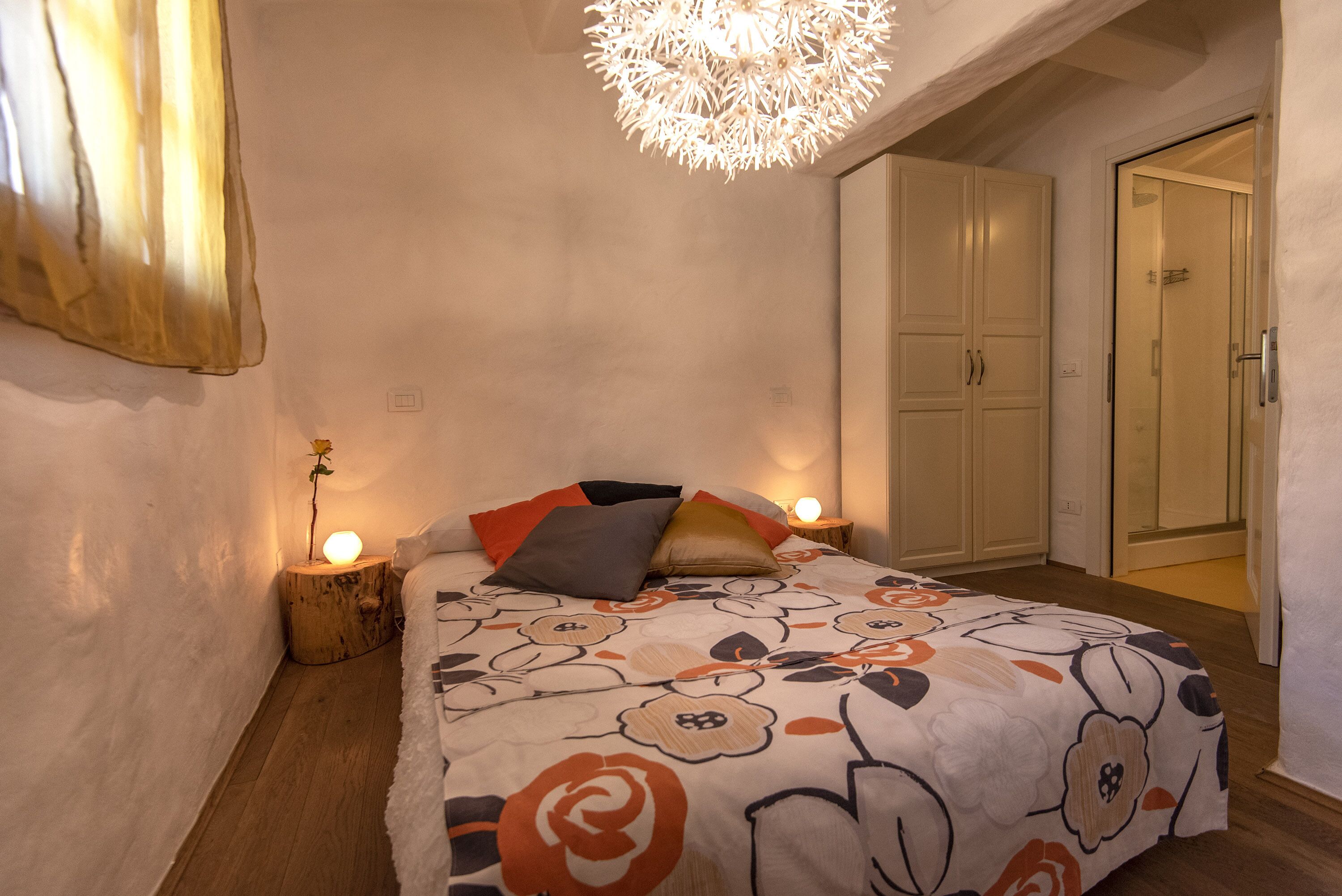 A bedroom with a floral bedspread, bedside lamps, a wooden nightstand, and a ceiling light fixture.